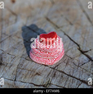 Una rosa e rosso cuori in ceramica piramide è posto su una superficie di legno piana e. Foto Stock