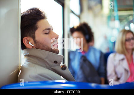 Imprenditore napping e ascoltando gli auricolari sul treno Foto Stock