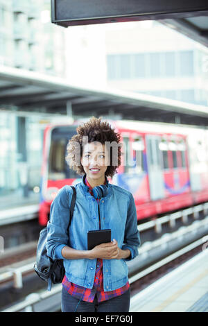 Donna che mantiene digitale compressa in una stazione ferroviaria Foto Stock