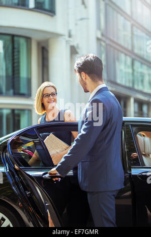 Chauffeur apertura porta auto per imprenditrice Foto Stock