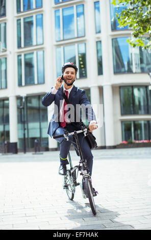 Imprenditore parlando al cellulare in bicicletta Foto Stock