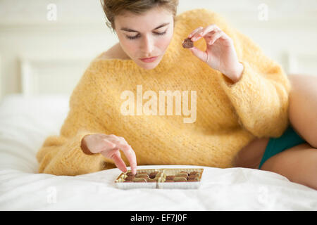 Donna mangiare il cioccolato sul letto Foto Stock