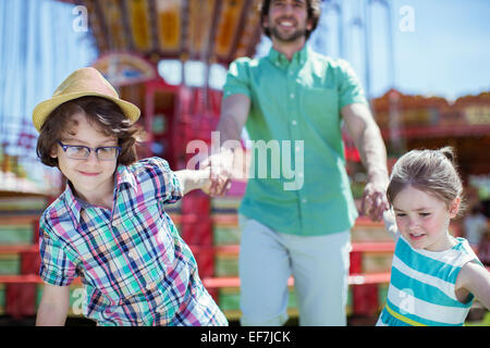 Ragazzo e una ragazza tirando il loro padre nel parco di divertimenti Foto Stock