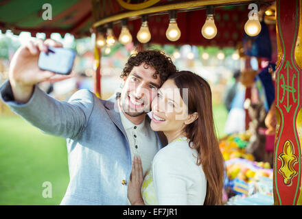 Coppia sorridente tenendo selfie nel parco di divertimenti Foto Stock