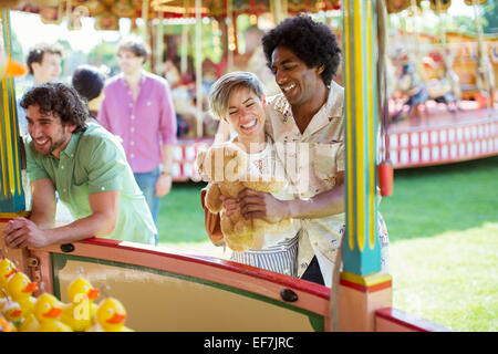 Sorridente giovane azienda orsacchiotto accanto al gioco della pesca nel parco di divertimenti Foto Stock