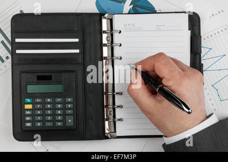 Diario, calcolatrice, mano e penna su uno sfondo di diagrammi e grafici Foto Stock