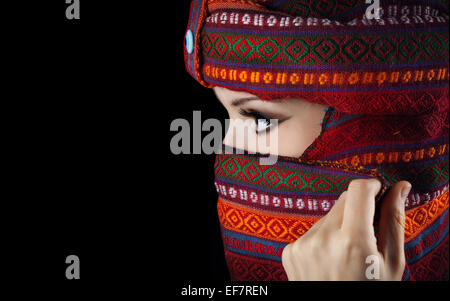 Donna orientale in turbante che copre il volto su sfondo nero Foto Stock