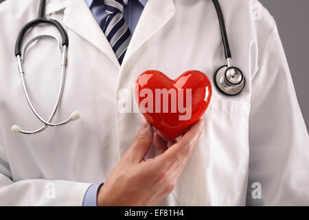 Medico tenendo cuore contro il petto Foto Stock