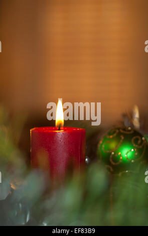 Red christmas candle burning, circondato da una corona di fiori e decorazioni Foto Stock