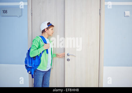 Pre-teen schoolboy apertura porta in aula e guardando all'interno Foto Stock
