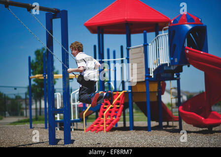 Ragazzo (10-11) oscillanti su swing sul parco giochi Foto Stock