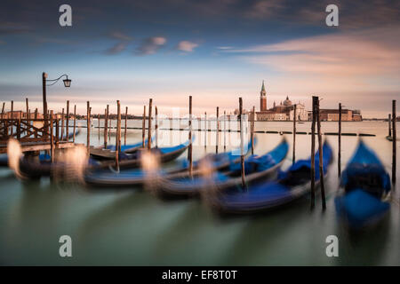 L'Italia, Venezia, gondole attraccate in fila con vista sullo skyline di distanza Foto Stock