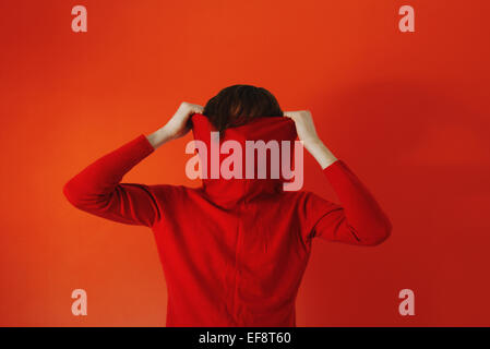 L'uomo tirando maglione rosso sulla faccia contro lo sfondo rosso Foto Stock