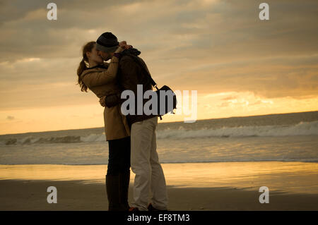 Paio di abbracciare e baciare sulla spiaggia al tramonto Foto Stock