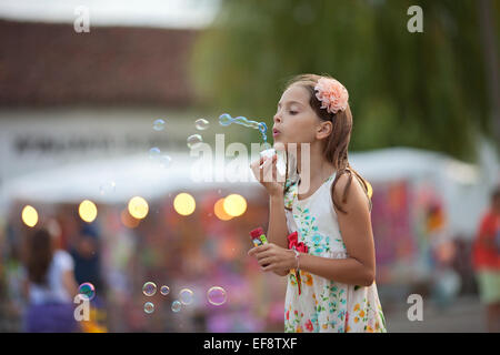 La ragazza (8-9) nel vestire soffiando bolle di sapone Foto Stock