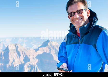 Uomo sorridente che tiene il telefono cellulare, Grand Canyon, Arizona, Stati Uniti Foto Stock