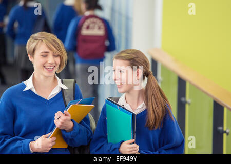 Due sorridenti studentesse indossano uniformi di scuola a piedi attraverso il corridoio della scuola Foto Stock