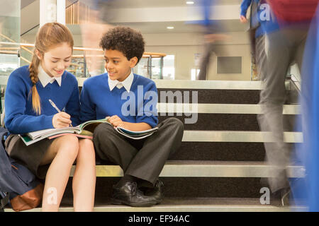 I bambini delle elementari che indossano uniformi di scuola seduti sui gradini e la scrittura nei libri di testo Foto Stock