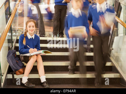 Ritratto di sorridente scuola elementare ragazza seduta sui gradini nella scuola Foto Stock
