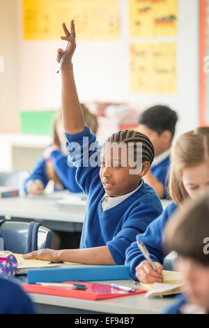 I bambini delle elementari in classe durante la lezione, ragazza alzando la mano Foto Stock