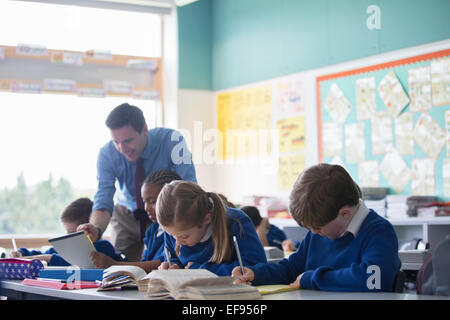 Insegnante maschio ad assistere i bambini delle elementari in classe durante la lezione Foto Stock