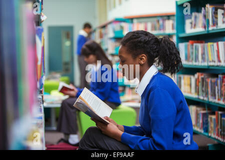 Gli studenti delle scuole superiori la seduta e la lettura di libro in biblioteca Foto Stock