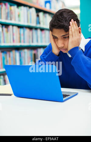 Ritratto di preoccupato studente cerca sul computer portatile in biblioteca Foto Stock