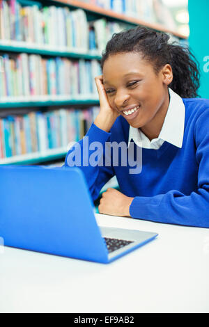 Sorridente studentessa guardando il laptop in biblioteca Foto Stock