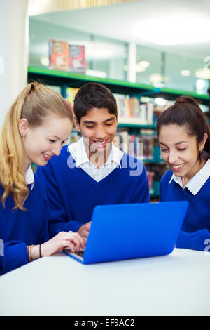 Tre allegri gli studenti a lavorare con il computer portatile nella libreria Foto Stock