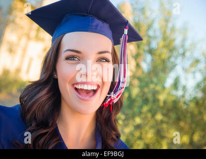 Felice la laurea razza mista donna nel cappuccio e camice celebrando in campus. Foto Stock