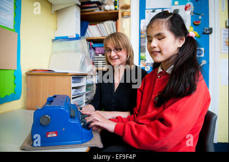 Ragazza cieca con insegnante e macchina da scrivere braille in particolari esigenze di classe a Londra la scuola primaria Foto Stock