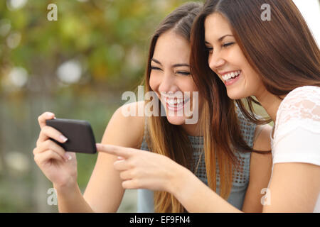 Due donne divertenti amici di ridere e di condivisione sociale dei media video in uno smart phone all'aperto Foto Stock