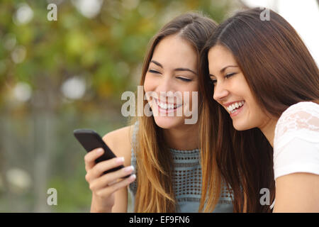 Due felici donne amici di condivisione sociale dei media in uno smart phone all'aperto in un parco Foto Stock