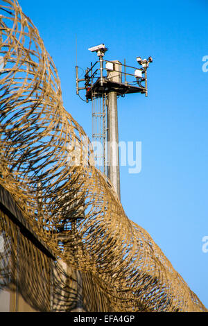 Incorniciato da recinzione internazionali per Stati Uniti/Messico bordo opposto alla Colonia Libertad distretto di Tijuana, una televisione torre di avvistamento sondaggi tentativi di immigrazione illegale. Nota il filo di rasoio sulla parte superiore della recinzione. Foto Stock