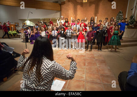 Multirazziale giovani bambini cantano canzoni natalizie, durante la messa di Natale a San Timoteo della Chiesa Cattolica, Laguna Niguel, CA. Nota direttore del coro. Foto Stock