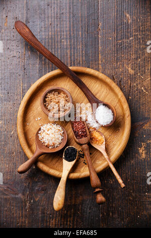 Diversi tipi di alimenti sale grosso in cucchiai di legno su sfondo scuro Foto Stock