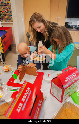 Un bambino la vita specializzato di choc ospedale per bambini in arancione, CA, contribuisce a una chemioterapia per il cancro del paziente e sua sorella fare una casa di panpepato. La vita del bambino il supporto di specialisti i pazienti e le loro famiglie in ambiente ospedaliero. "Nota I.V. tree". Foto Stock