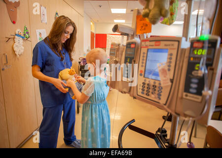 Un bambino la vita specializzato di choc ospedale per bambini in arancione, CA,mostra un 'chemo duck' per una giovane ragazza in chemioterapia paziente di cancro. L anatra dimostra il posizionamento di un tubo flessibile per via endovenosa 'porta' per farmaci di chemioterapia bambino vita il supporto di specialisti i pazienti e le loro famiglie in ambiente ospedaliero. Nota testa calva e supporto per via endovenosa con il computer. Foto Stock