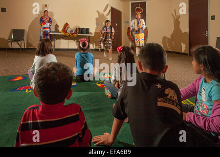 Come figli del pubblico orologio e un 7-anno-vecchio Indiano Navajo indossando ballerino completo costume tribale esegue il jingle Dress ballare durante una serata di Native American cultura presso la Laguna Niguel, CA, biblioteca pubblica. Nota padre in costume e la sorella. Foto Stock