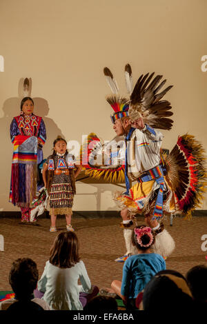 Come figli del pubblico guarda, un Indiano Navajo indossando ballerino completo costume tribale esegue la fantasia del tuono ballare durante una serata di Native American cultura presso la Laguna Niguel, CA, biblioteca pubblica. Nota figlie in costume. Foto Stock