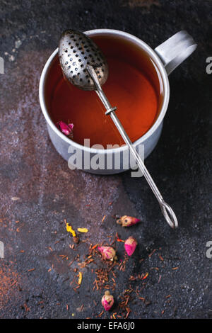 Alluminio Vintage tazza di tè caldo con filtro di tè, tè secco e boccioli di rosa su sfondo scuro. Vista superiore Foto Stock