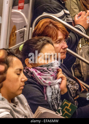 Una donna con un freddo si copre la bocca con una sciarpa mentre si è in viaggio in un vagone della metropolitana di New York City. Foto Stock