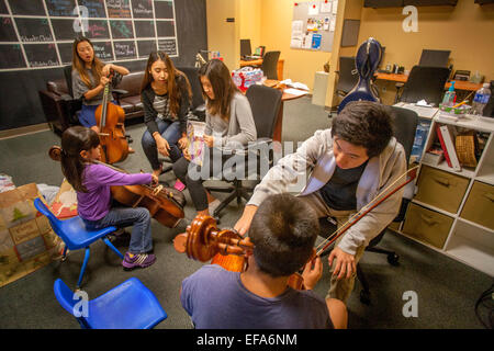 Asian alta scuola di musica di volontariato mentor insegnare violoncello per bambini ispanico presso un centro comunitario in Santa Ana CA. Nota azienda mentor spartiti di musica per la ragazza per giocare. Foto Stock