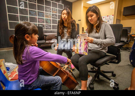 Asian alta scuola di musica di volontariato mentor insegnare violoncello per bambini ispanico presso un centro comunitario in Santa Ana CA. Nota teen ragazza con foglio di musica per la ragazza per giocare. Foto Stock