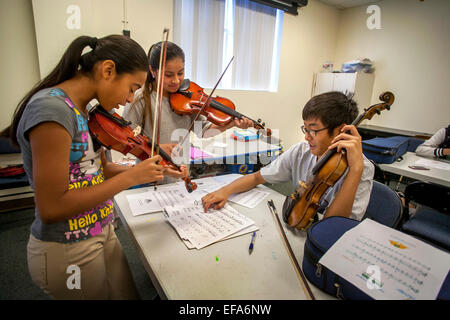 Un asiatico di alta scuola di musica di volontariato mentor insegna violino a ispanica ragazze adolescenti a una community center di Santa Ana CA. Nota spartiti. Foto Stock