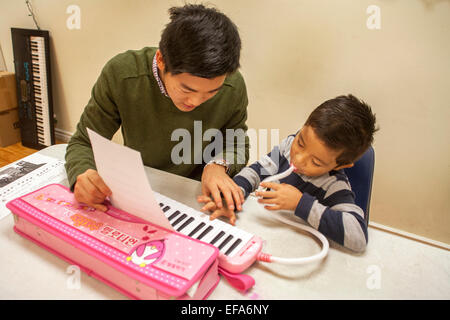 Un asiatico di alta scuola di musica di volontariato mentor insegna un ragazzo Ispanico per riprodurre la melodica presso un centro comunitario in Santa Ana CA. Nota spartiti. La melodica, noto anche come pianica, blow-organo o key-flauto, è un Free-reed strumento con una tastiera sulla parte superiore e viene svolto mediante insufflazione di aria attraverso un boccaglio. Foto Stock