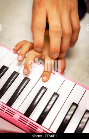 Un asiatico di alta scuola di musica di volontariato mentor guida la mano di un ragazzo Ispanico per riprodurre la melodica presso un centro comunitario in Santa Ana CA. La melodica, noto anche come pianica, blow-organo o key-flauto, è un Free-reed strumento con una tastiera sulla parte superiore e viene svolto mediante insufflazione di aria attraverso un boccaglio. Foto Stock