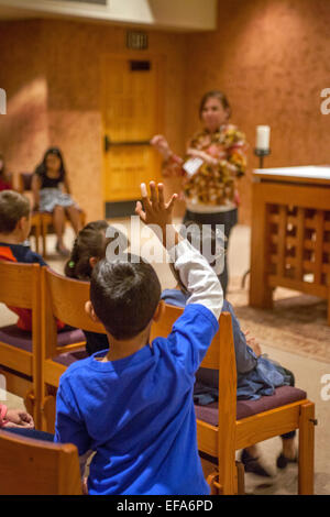 Un ragazzo alza la mano per rispondere a una domanda a una lezione religiosa di multirazziale giovani bambini noto come Tiny Tim nella cappella di San Timoteo della Chiesa Cattolica, Laguna Niguel, CA. Nota insegnante. Foto Stock