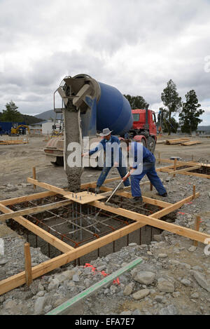 Un team di costruttori dirige il calcestruzzo bagnato da un camion di cemento nelle fondamenta di un edificio di grandi dimensioni Foto Stock