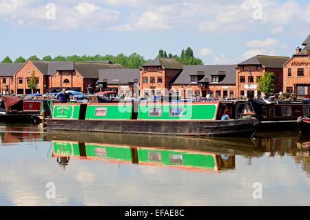 Narrowboats sulla loro ormeggi nel bacino del canale con negozi, bar e ristoranti per la parte posteriore, Barton Marina, Inghilterra. Foto Stock